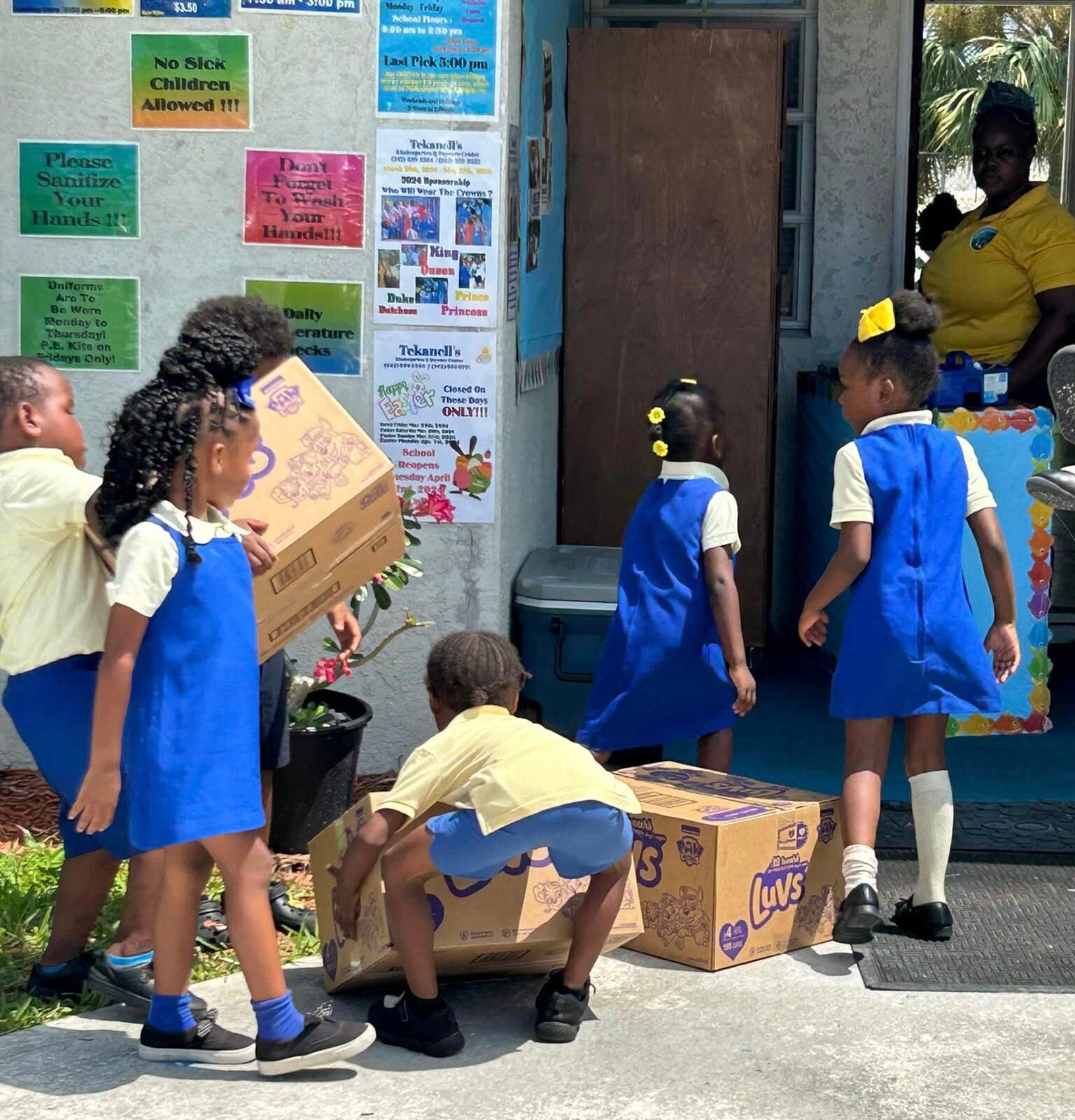 Children helping carry household supplies into the preschool they attend