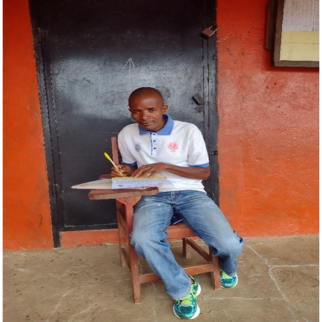 Joshua, a teacher in Liberia, sitting at a school desk