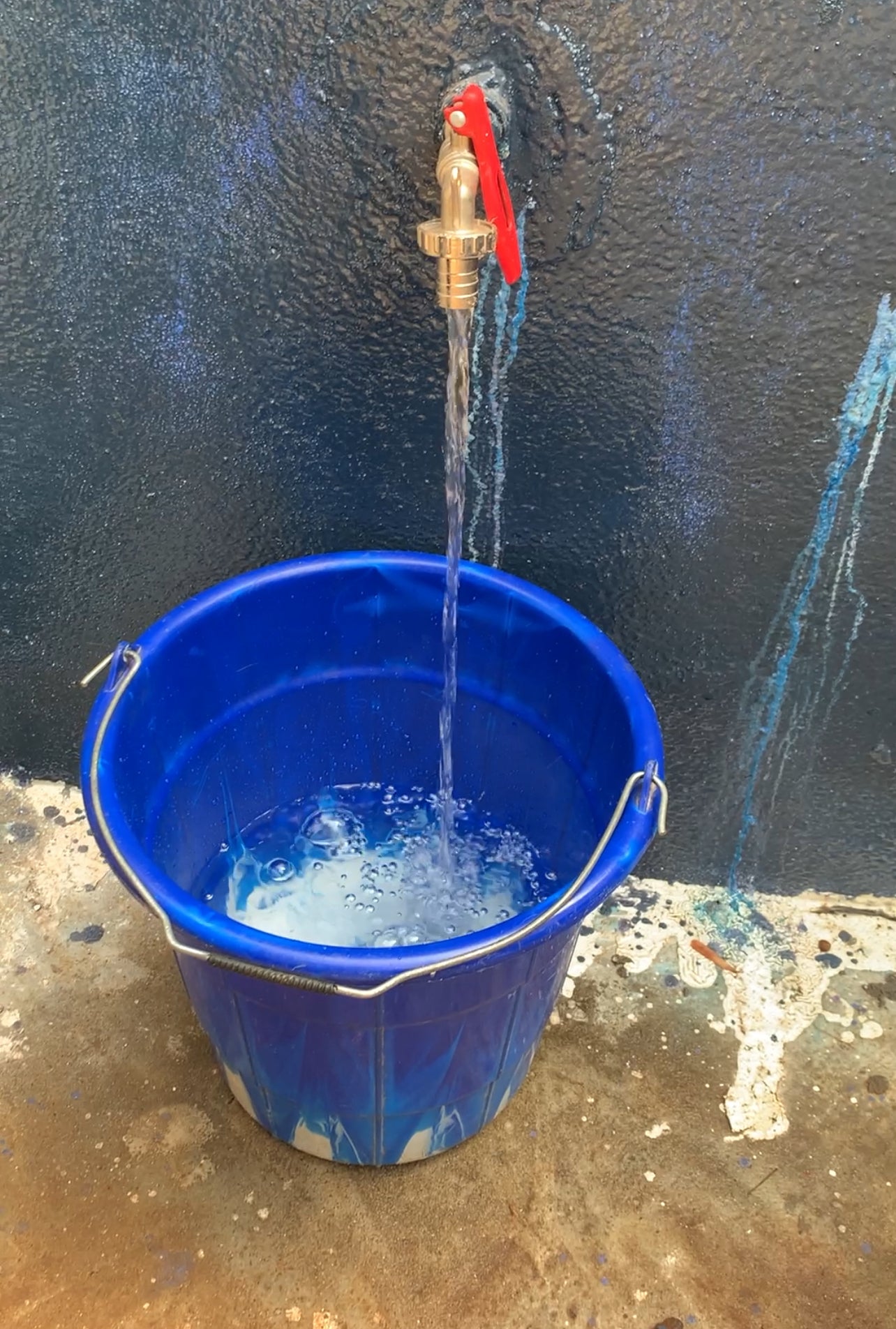 Water flowing from a tap into a blue bucket